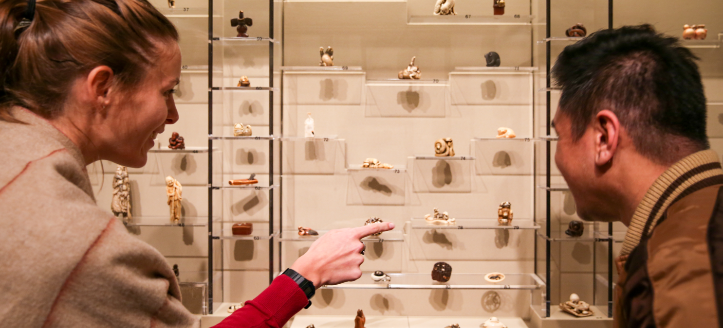 A man and a woman look closely at a case filled with netsuke.