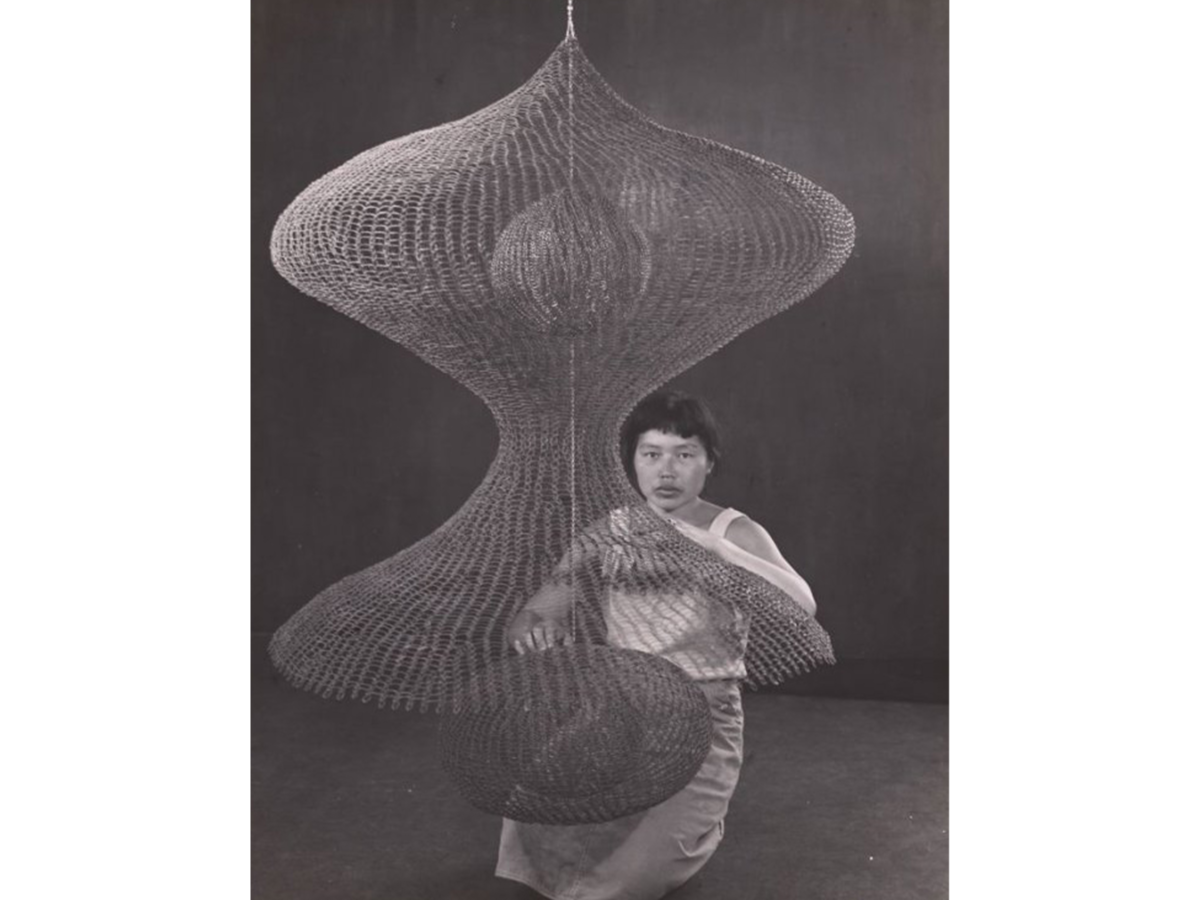 Ruth Asawa standing with one of her woven hangings.