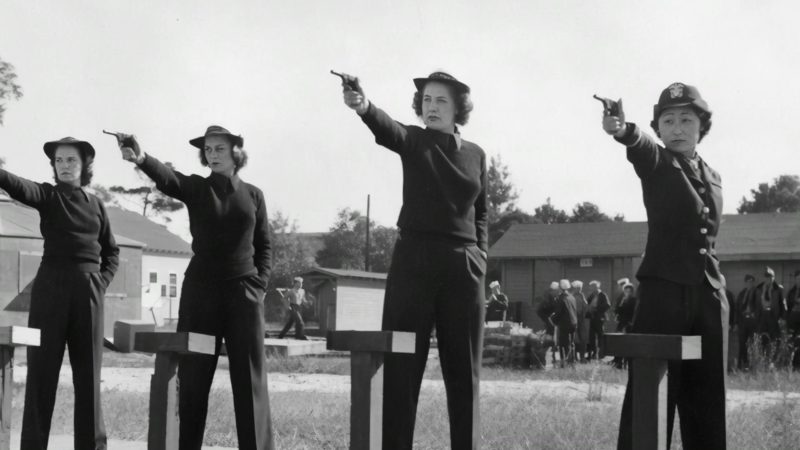 Four women in uniform holding small pistols.