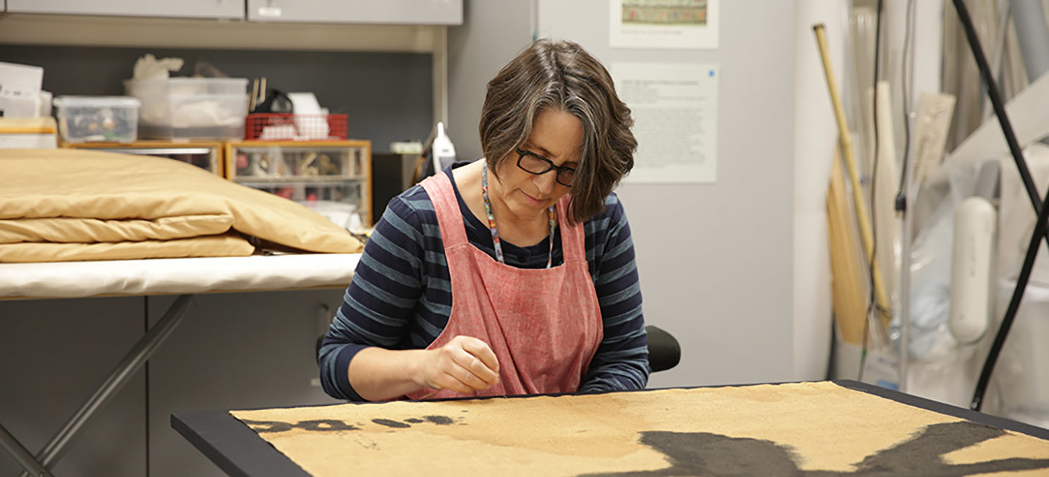 A conservator works on a textile.